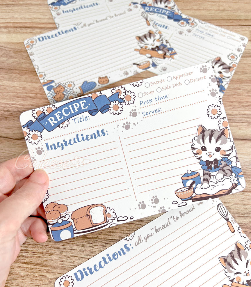 Set of recipe cards with cat-themed illustrations on a wooden surface.