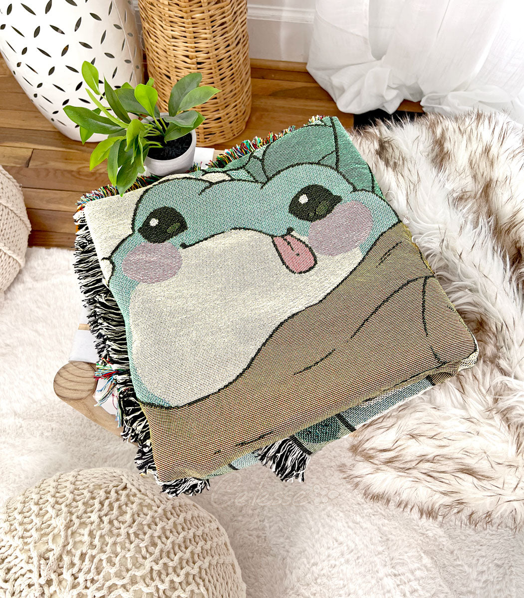 A woven blanket featuring blob-like frogs folded into a square and set on a bench in a cozy beige bedroom setting.