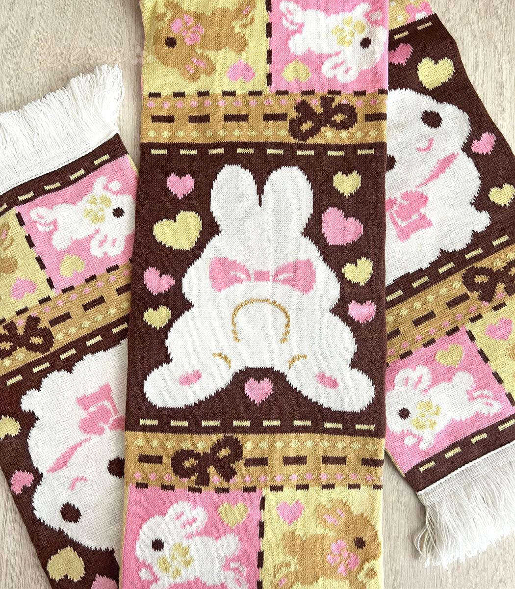 A knit scarf with a patchwork bunny pattern laid on a wooden surface. The featured section shows a bunny sploot.