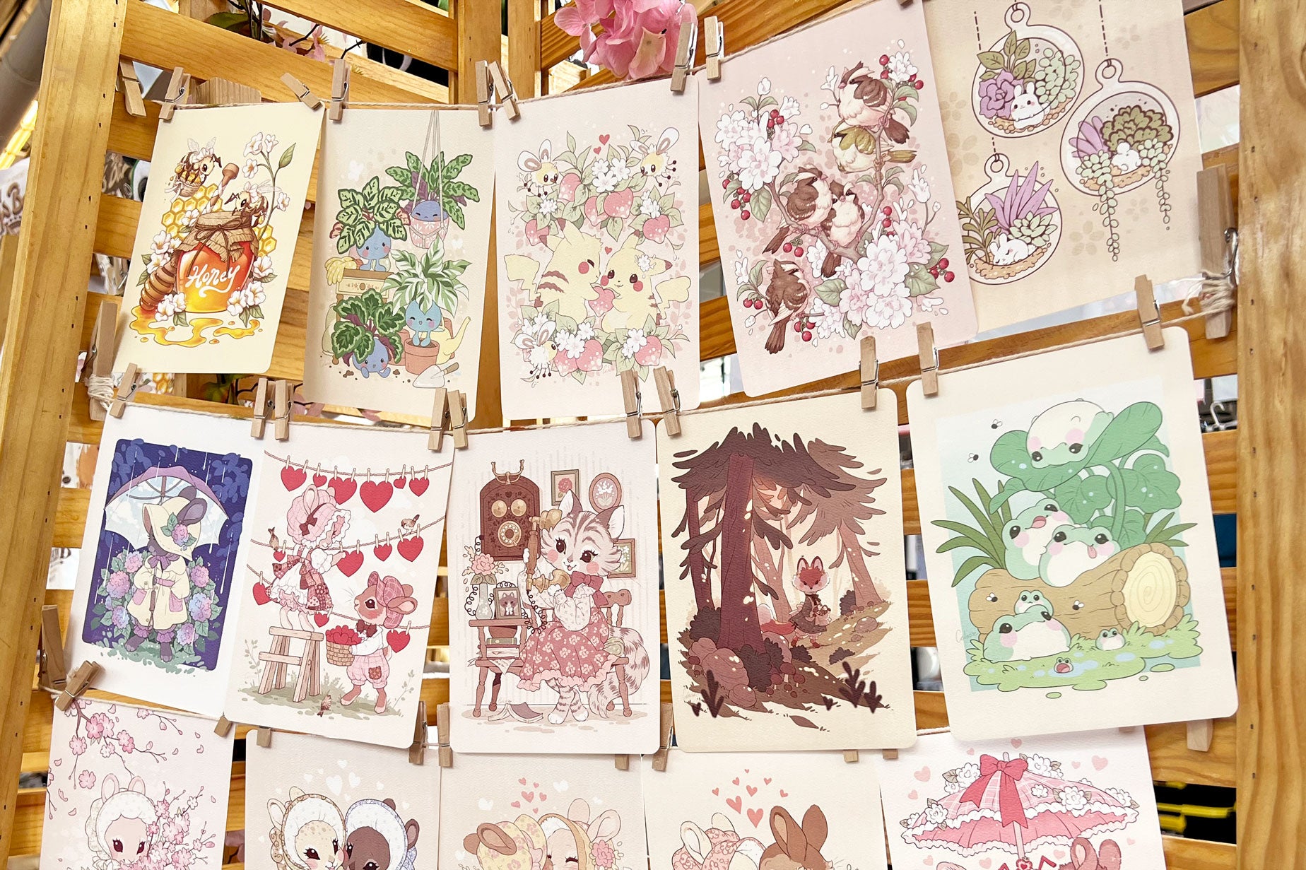 A photo of a large display of textured prints featuring soft, vintage-style art, strung up on twine with clothes pins.