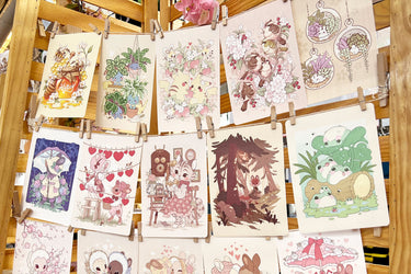A photo of a large display of textured prints featuring soft, vintage-style art, strung up on twine with clothes pins.