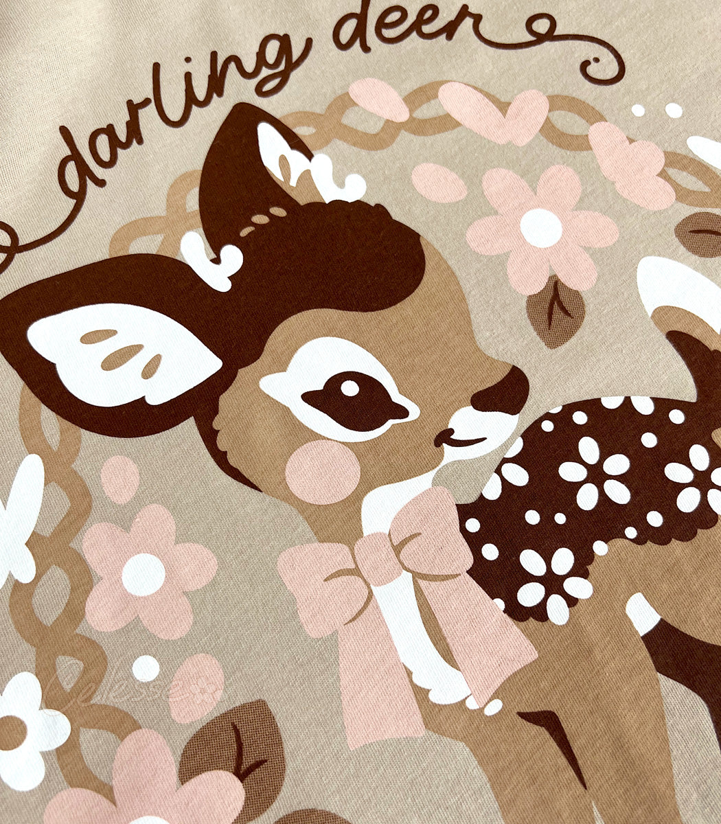 Close up photo of the print of a shirt featuring a baby deer with floral elements on a tan background.