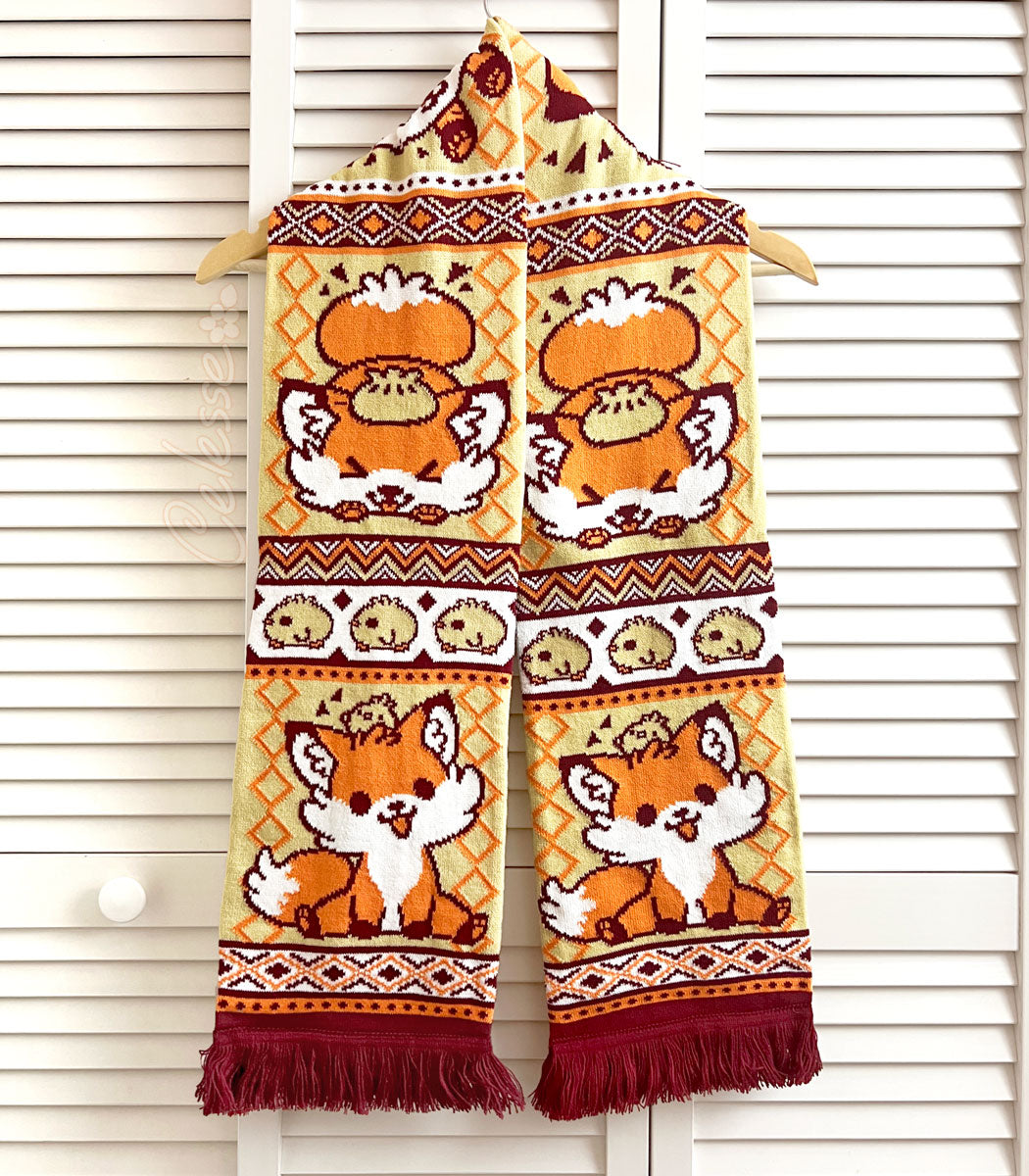 A photo of a fox-themed knit scarf with intricate patterns hanging against a white slat wall background.