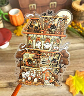 Photo of a clear vinyl sticker with artwork of a decorative Halloween-themed house full of witch cats over a wooden surface with pumpkins and leaves.