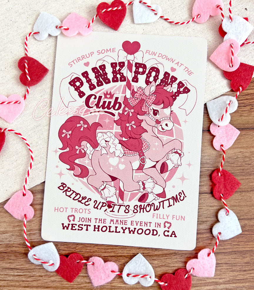 An art print on a table decorated with a string of hearts with a logo for Pink Pony Club, the art featuring a prancing pink pony in frilly décor. The flavor text reads "Bridle up, it&