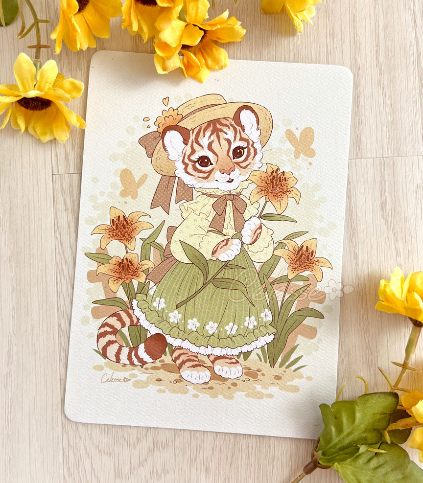 A photo of an art print featuring a tigress in a garden of tiger lilies and wearing a spring dress and straw hat.