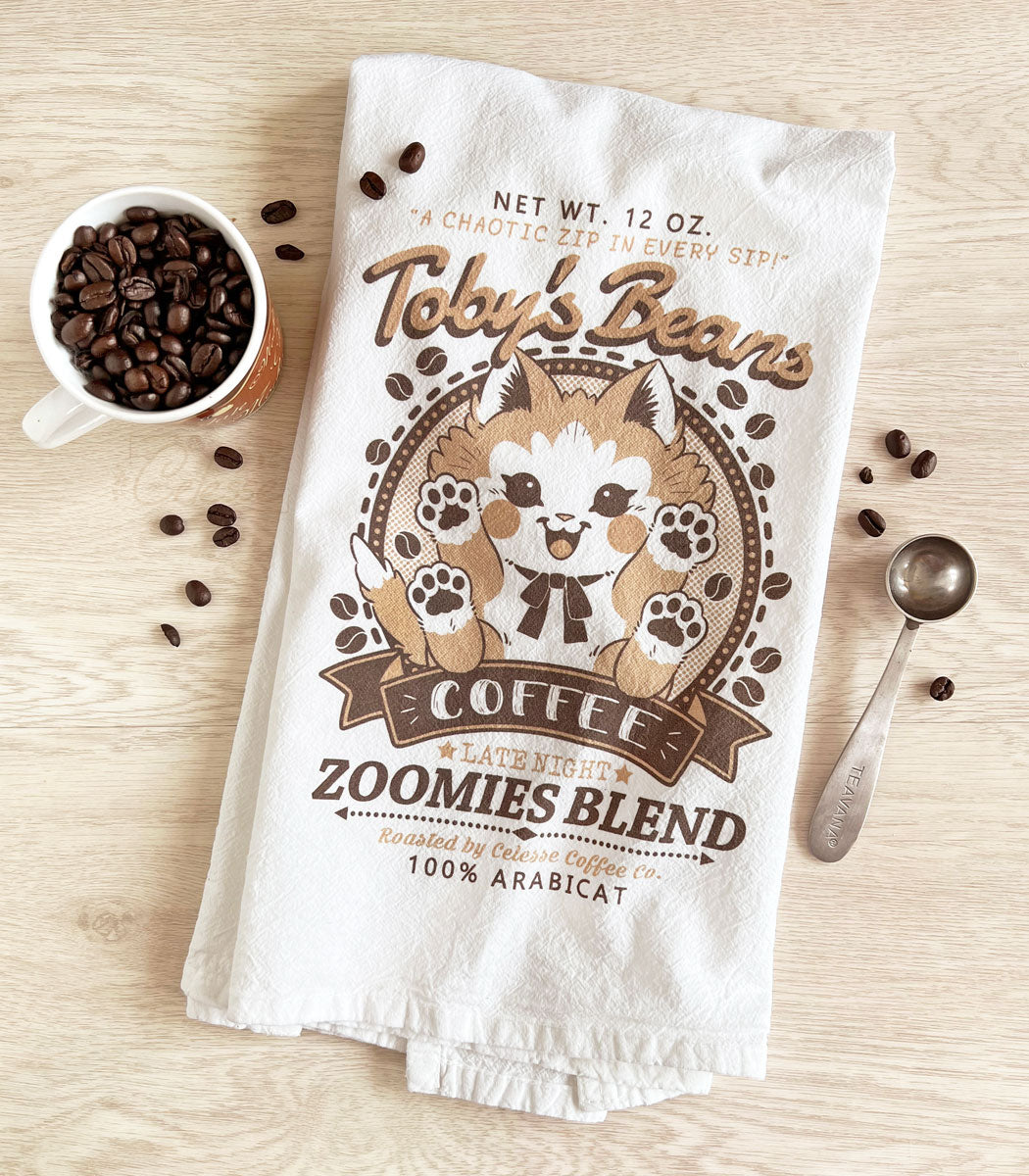 A photo of a flour sack tea towel on a wooden table, the print is a faux vintage-style logo for Toby&
