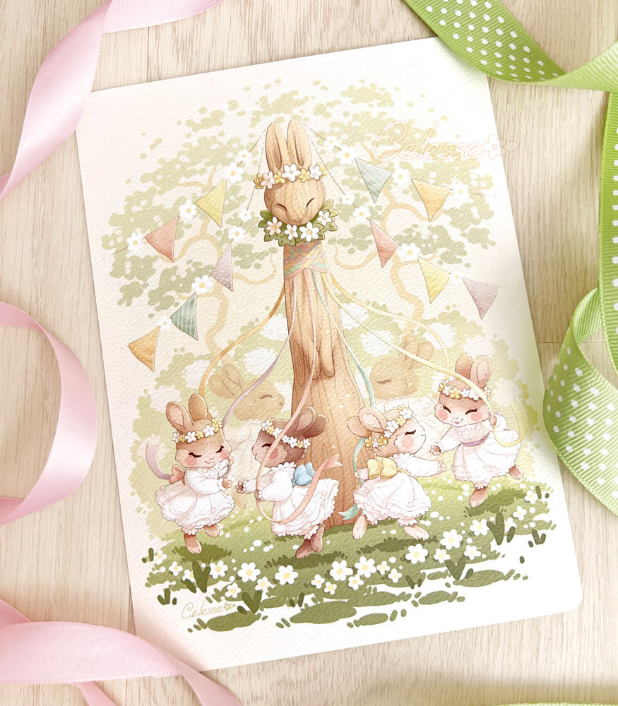 A photo of a textured art print featuring a soft springtime illustration set in a sunny glade, a group of young bunny girls in frilly white dresses and flower crowns prancing around a tall wooden maypole carved in the shape of a rabbit. Each girl holds a ribbon and reaches for the paw of the next girl as they dance, braiding the ribbons around the neck of the maypole. Colorful flags are strung from the top of the pole and flowering trees, bushes and grass decorate the background.