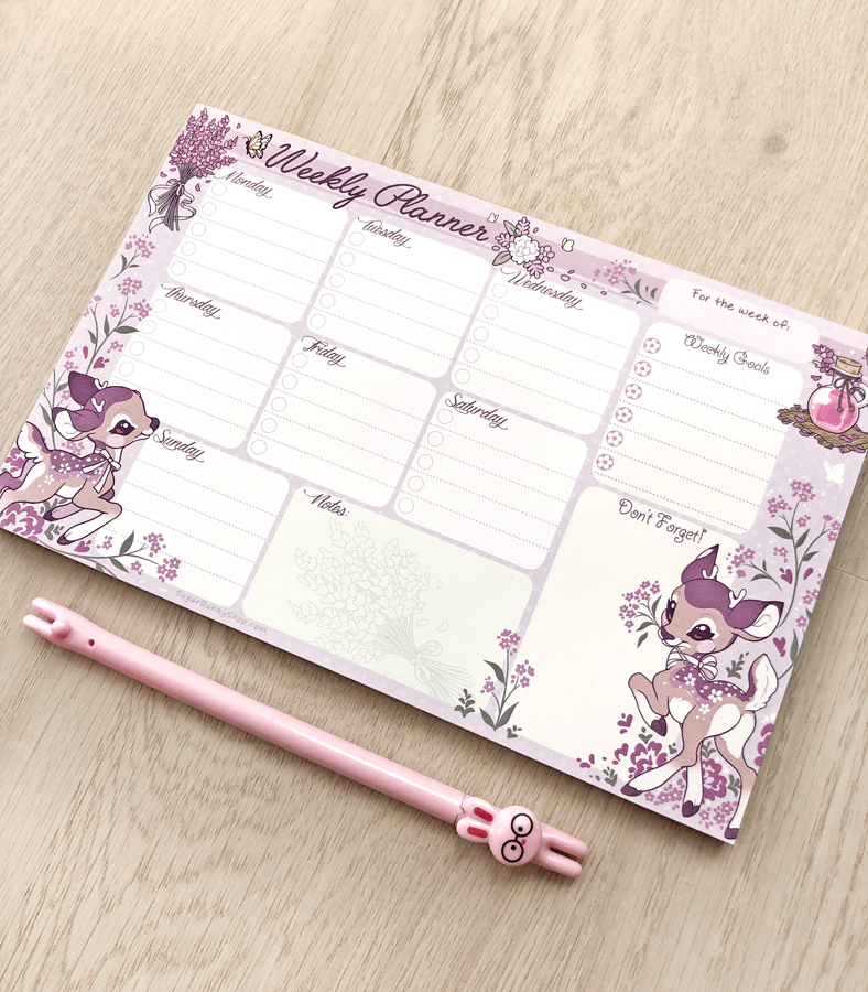 A photo of a weekly planner notepad on a wood table, the design featuring a lavender theme with cute baby deer frolicking around task sections for each day of the week, as well as extra sections for notes and goals.