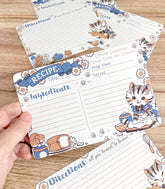 Set of recipe cards with cat-themed illustrations on a wooden surface.
