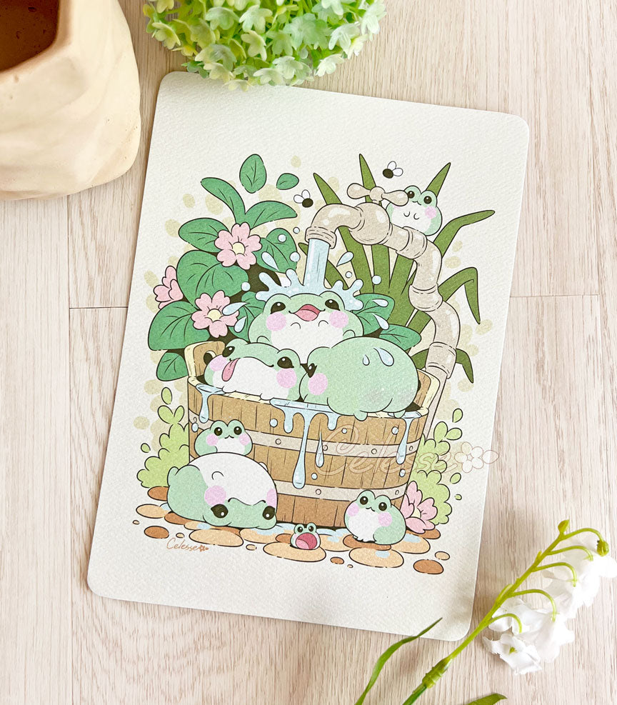 A photo of an art print featuring blob frogs splashing around in a garden bucket.