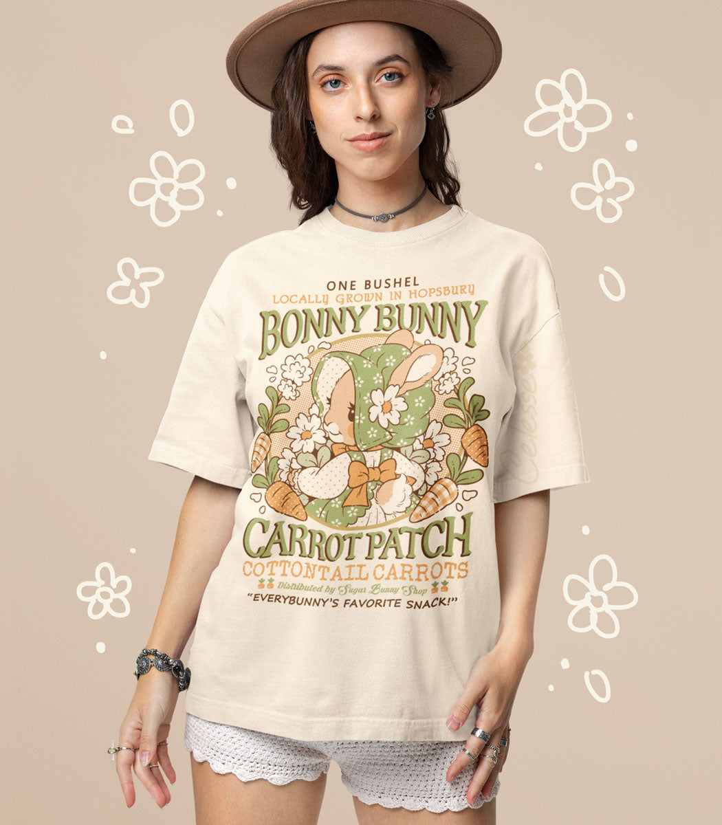 A photo of a girl wearing a natural colored shirt, the printed design featuring a vintage-style logo for Bonny Bunny Carrot Patch with a bunny in a floral bonnet and dress, holding a bundle of flowers and wreathed by carrots.