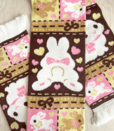 A knit scarf with a patchwork bunny pattern laid on a wooden surface. The featured section shows a bunny sploot.
