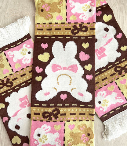 A knit scarf with a patchwork bunny pattern laid on a wooden surface. The featured section shows a bunny sploot.