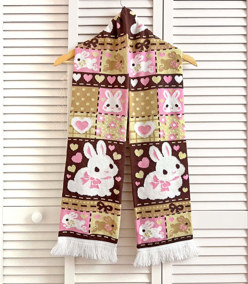 A knit scarf with a patchwork bunny pattern in Neapolitan colors hanging on a white slat wall background.