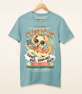 A dusty blue shirt on a wood hanger with a print of a vintage-style logo for Chasing Rays Sun Lotion, the art featuring an energetic, floppy-eared dog wearing a bandana and sunglasses. The flavor text reads, "Sun&