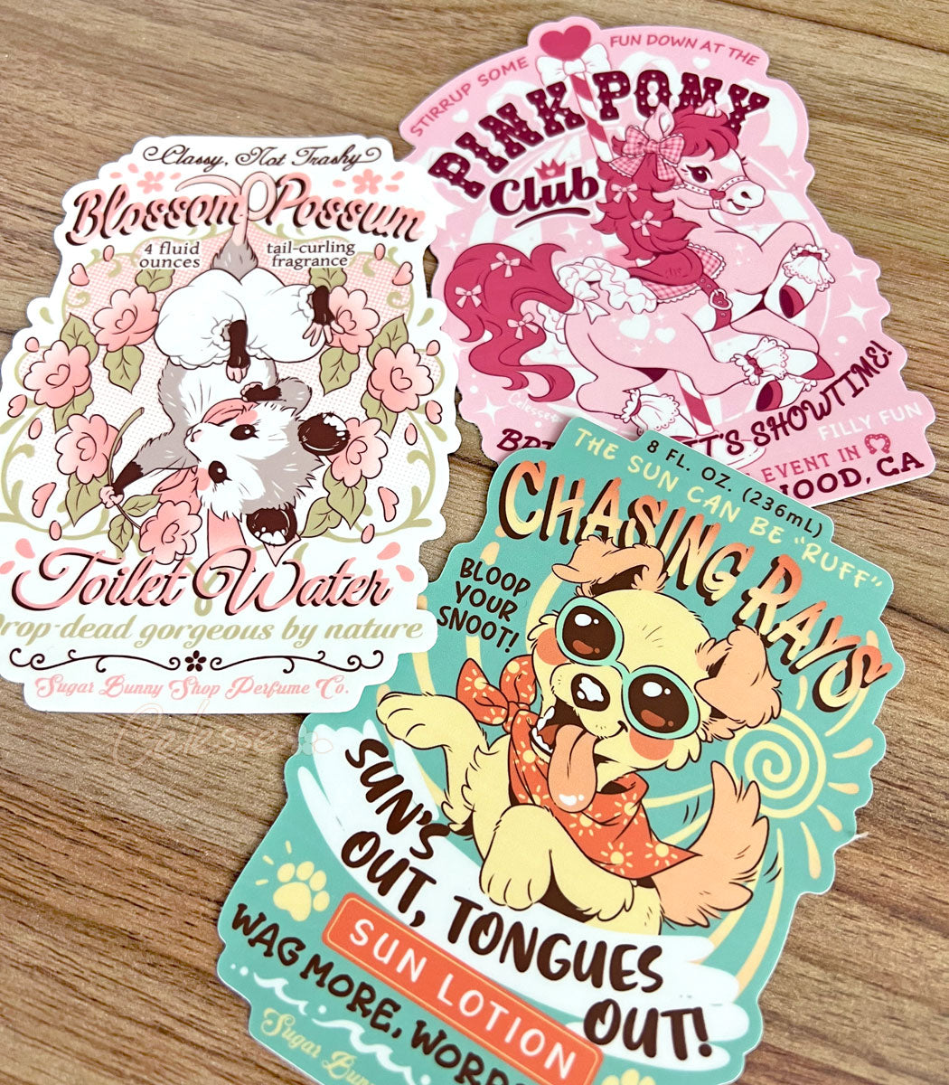 Three large vinyl stickers on a wood table, each design a different vintage-style logo for various faux products, the art featuring cute animal mascots.