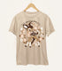 A tan-colored shirt on a wood hanger featuring a print of a baby deer with flower spots, surrounded by a wreath. The text reads "darling deer".