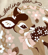 Close up photo of the print of a shirt featuring a baby deer with floral elements on a tan background.