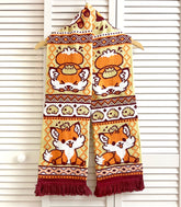 A photo of a fox-themed knit scarf with intricate patterns hanging against a white slat wall background.