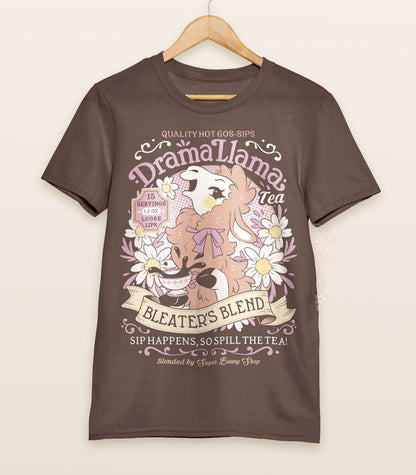 A brown shirt on a wood hanger with a print for a faux vintage-style logo for Drama Llama Tea, the art featuring a gossipy llama spilling the tea.