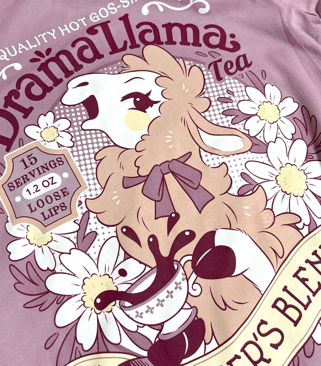 A close up photo of a muted lilac shirt with a print for a faux vintage-style logo for Drama Llama Tea, the art featuring a gossipy llama spilling the tea.