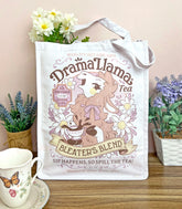 A white canvas tote bag with a gossipy llama surrounded by flowers in a vintage-style logo for "Drama Llama Bleater&