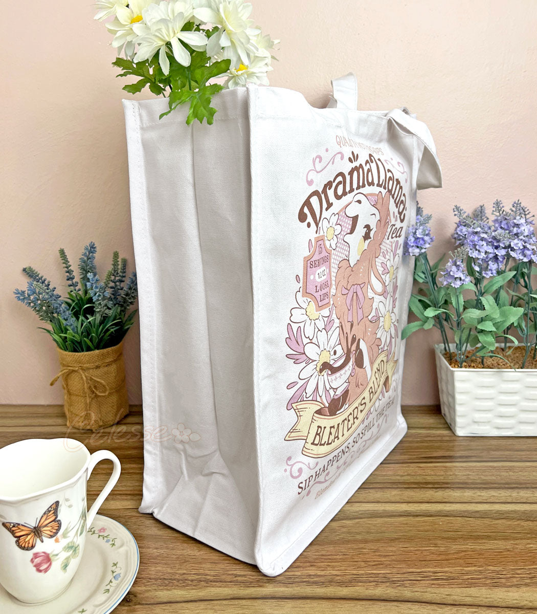 A side view white canvas tote bag with a gossipy llama surrounded by flowers in a vintage-style logo for "Drama Llama Bleater&