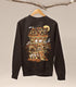 A dark brown sweatshirt on a wood hanger hung from a branch, the print featuring a Halloween-themed haunted home full of witch cats and ghosts.