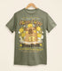A light olive green shirt on a wood hanger with a print of a vintage-style logo for Happy Cappy Yuzu Fruit, the center art featuring a smiling capybara in a hot spring.