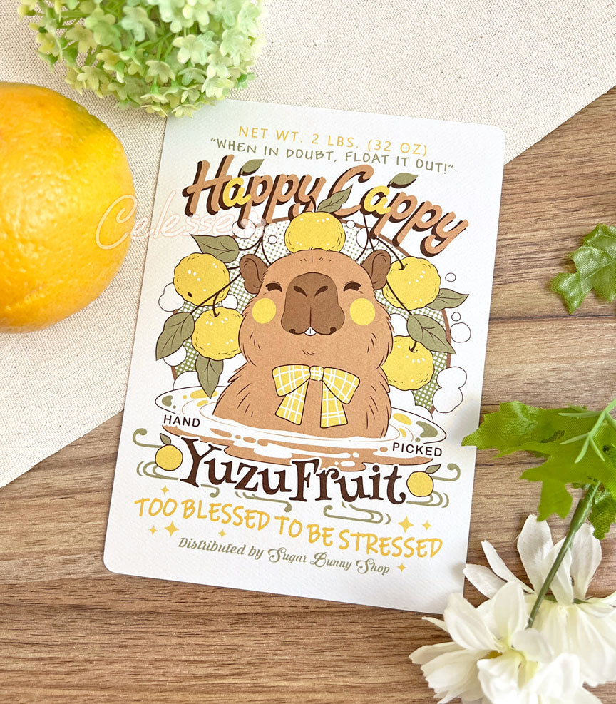 An art print of a vintage-style logo for Happy Cappy Yuzu Fruit, the illustration featuring a blissful-looking capybara sitting in a hot spring pool with yuzu spread around it. The secondary text reads "When in doubt, float it out!" and "Too blessed to be stressed."