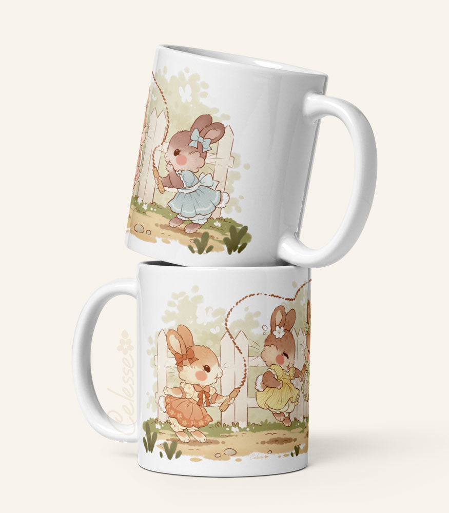 Two stacked ceramic mugs with a print featuring art of a bunch of bunny girls playing jump rope in vintage dresses.
