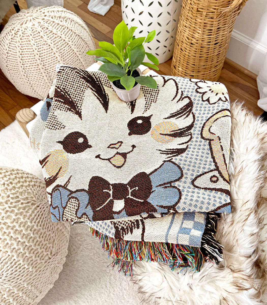 A photo of a folded woven blanket featuring an image of kitten&
