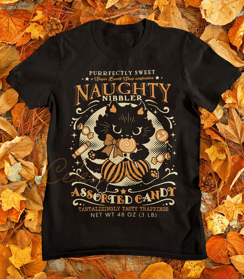 A photo of a black shirt featuring a vintage-style logo in orange and yellow for Naughty Nibbler Assorted Candy. A black kitten eating a lollipop prances among various candies between the text.