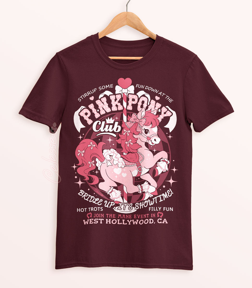 A maroon shirt on a wood hanger with a print of a logo for Pink Pony Club, the art featuring a prancing pink pony in frilly décor. The flavor text reads "Bridle up, it&