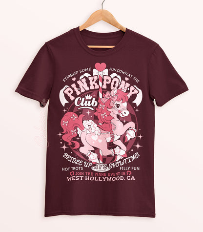 A maroon shirt on a wood hanger with a print of a logo for Pink Pony Club, the art featuring a prancing pink pony in frilly décor. The flavor text reads "Bridle up, it&