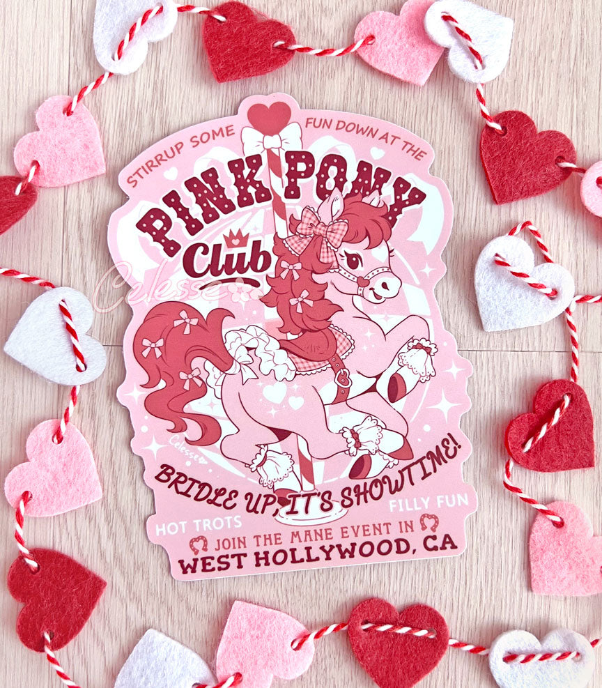 An extra large vinyl sticker on a table decorated with a string of hearts with a logo for Pink Pony Club, the art featuring a prancing pink pony in frilly décor. The flavor text reads "Bridle up, it&