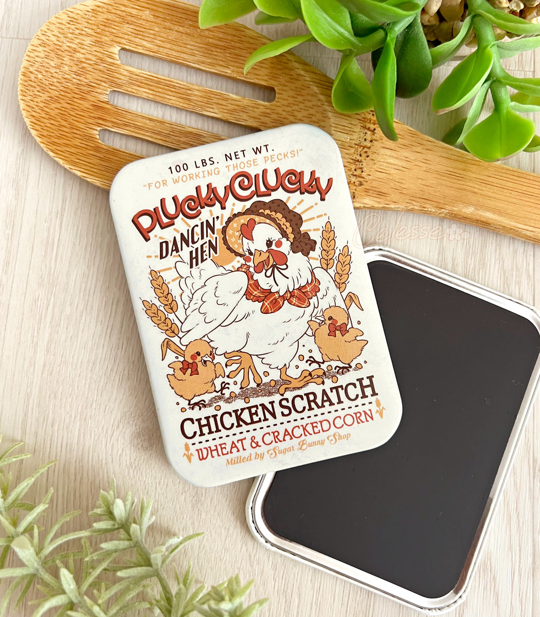 Chicken Scratch logo design fridge magnet with a wooden spoon and plants on a wood surface.