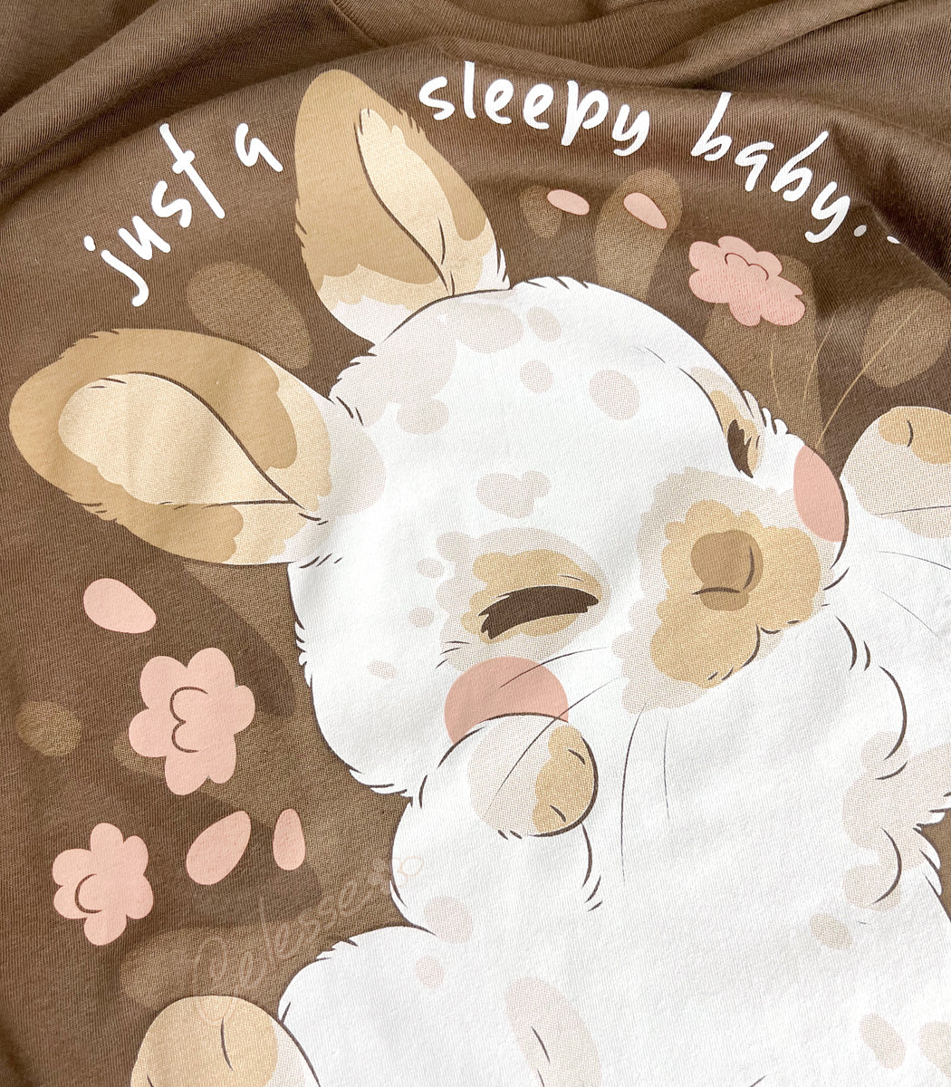 Close up photo of a shirt print featuring a baby bunny with flowers and text on a brown background.