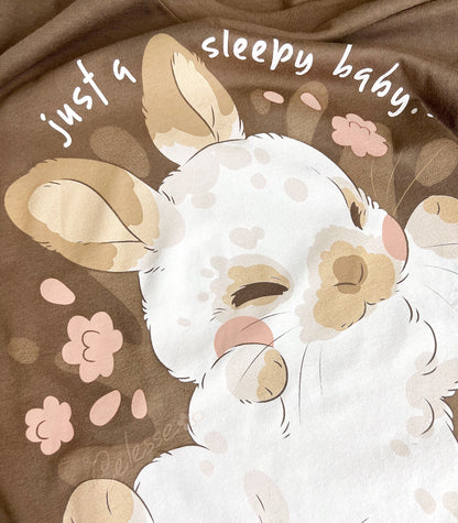 Close up photo of a shirt print featuring a baby bunny with flowers and text on a brown background.