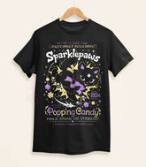 A black shirt on a wood hanger with a print of a retro faux candy logo for Sparklepaws Popping Candy, the art featuring a black cat with star paw pads leaping among bursting sparkles. The flavor text reads, "Dazzlingly delicious!" and "Frolic among the stardust!"