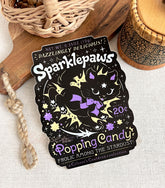 A vinyl sticker with a print of a retro faux candy logo for Sparklepaws Popping Candy, the art featuring a black cat with star paw pads leaping among bursting sparkles. The flavor text reads, "Dazzlingly delicious!" and "Frolic among the stardust!"