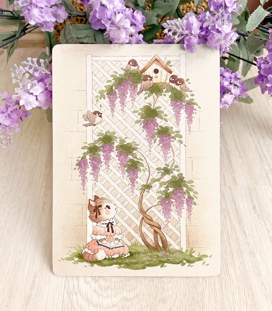 A photo of a textured art print on a light wood table with purple flowers above it. The print features a soft drawing of a kitten in a vintage-style dress who is in a garden with a book in her lap, sitting at the base of a tall white lattice wall with purple wisteria growing up it. A bird house perches at the top of the lattice and chickadees sing and flit about, luring the kitten&