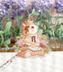 A photo of a clear vinyl sticker featuring artwork of a kitten reading a book in a vintage dress with birds, a basket of lavender flowers in the background.