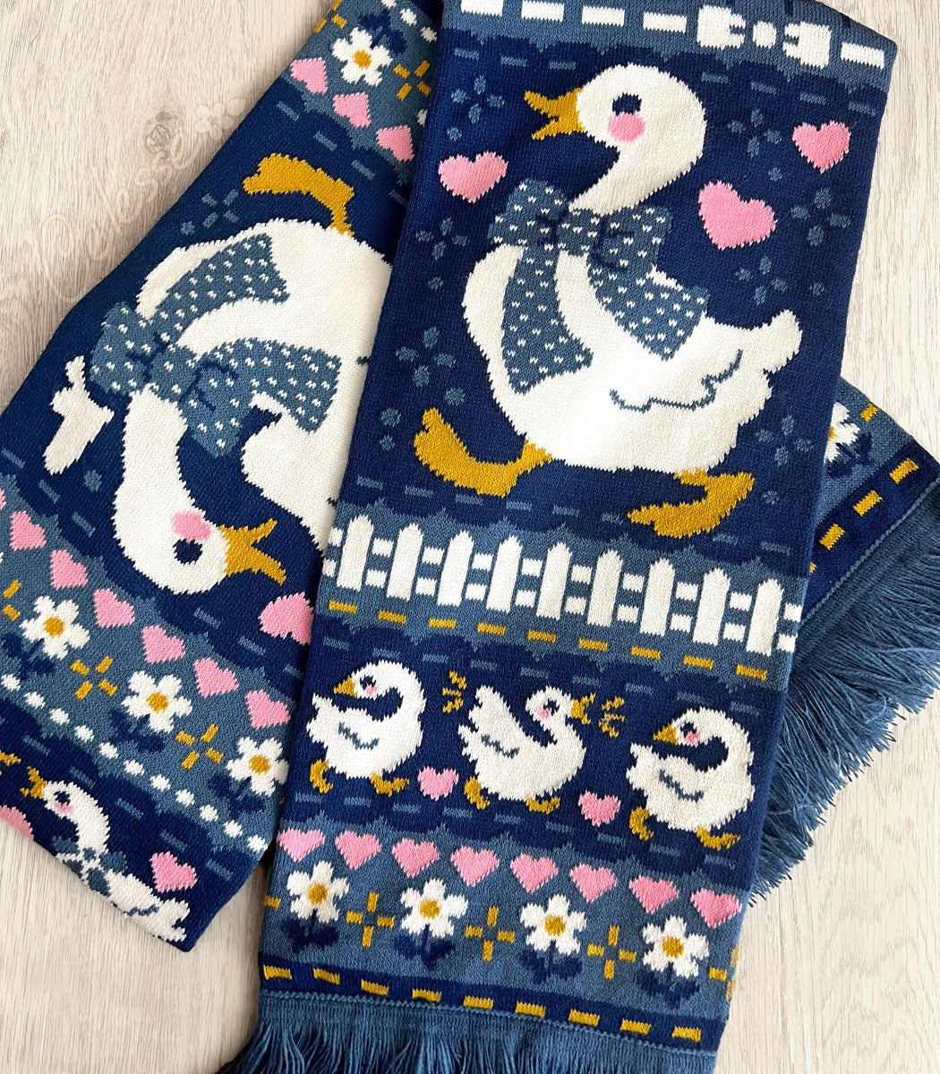 A blue knit scarf with a vintage-style goose design laid on a wooden surface.