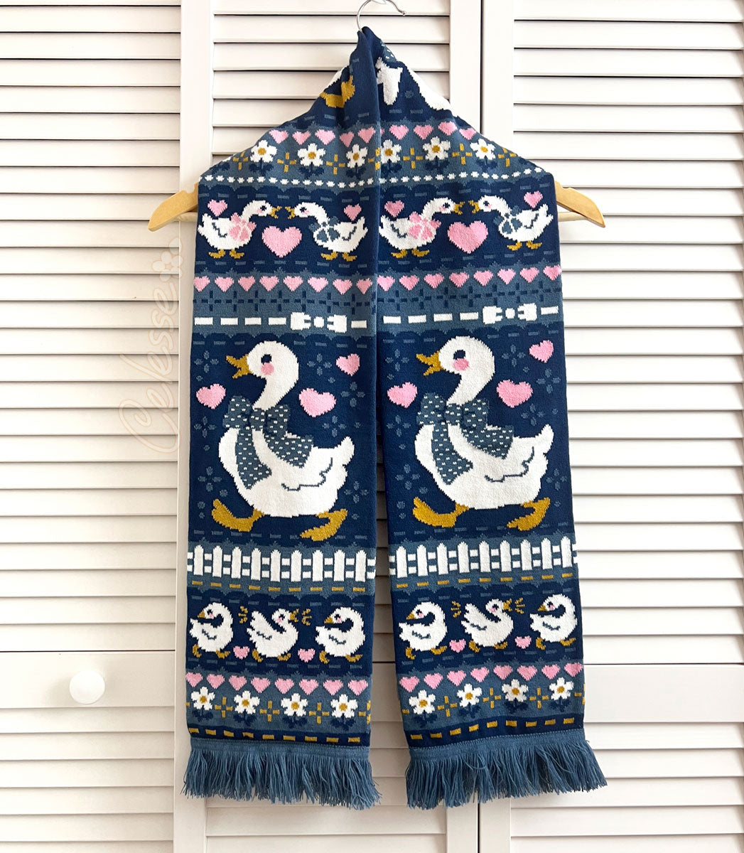 A blue knit scarf with a vintage-style goose design hanging on a white slat wall.