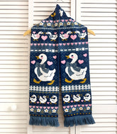 A blue knit scarf with a vintage-style goose design hanging on a white slat wall.