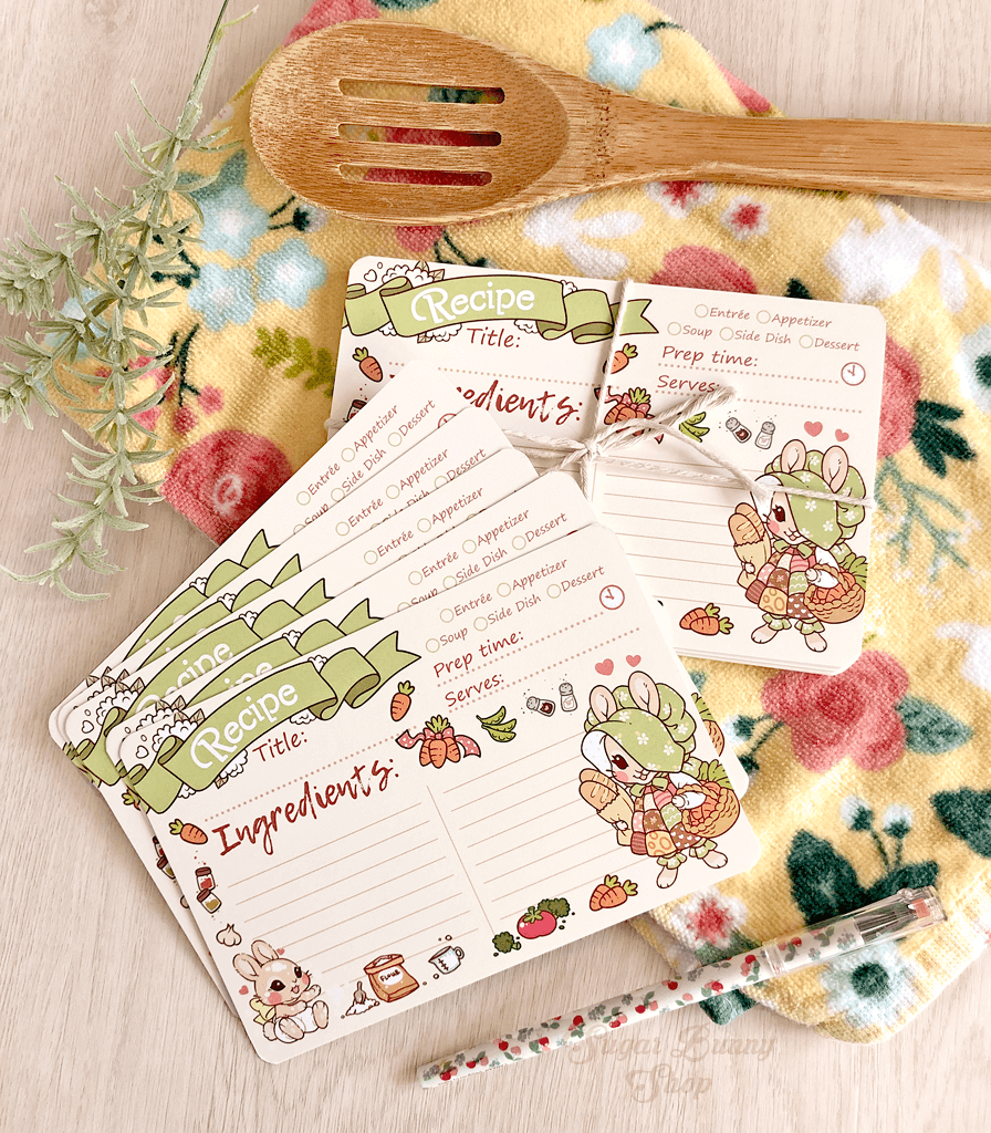 A photo of a batch of recipe cards featuring a vintage style bunny wearing a patchwork apron, random food and other cooking items scattered around the border of the cards.