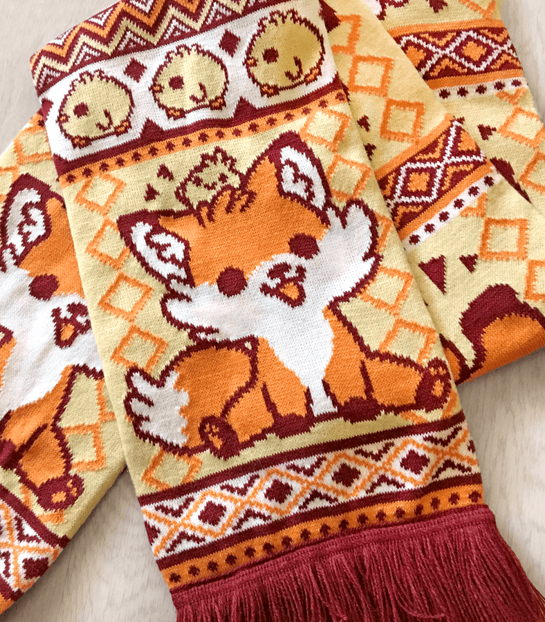 A knit scarf featuring a pattern with a fox and geometric shapes, predominantly in red and orange colors, with a fringe.