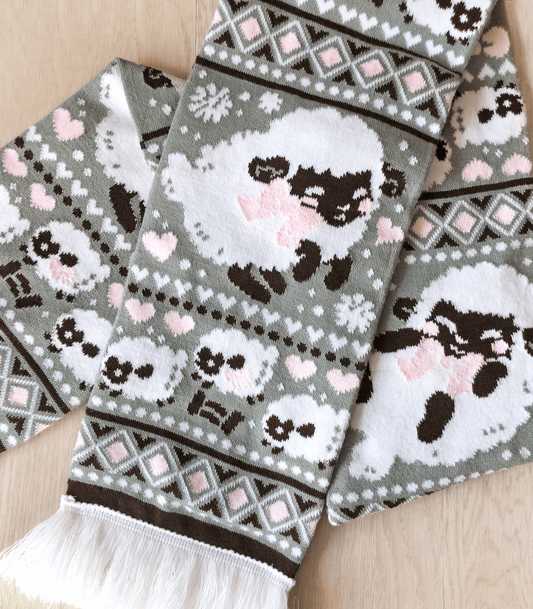 A photo of a knit scarf featuring fat fluffy white sheep with dark faces. The scarf is gray and white and has repeating knit patterns like diamonds, dots and hearts.